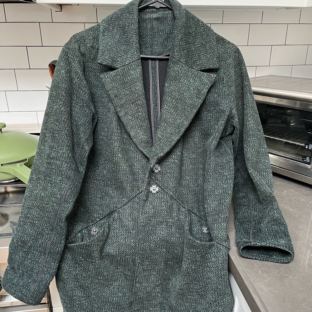 This is a lululemon cocoon coat in the color green with specs of black.